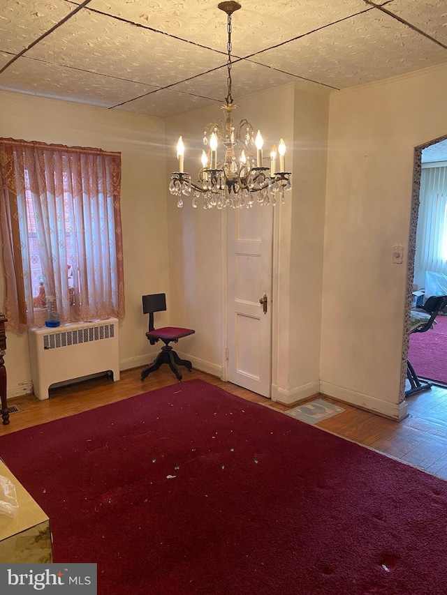 unfurnished dining area featuring a notable chandelier, radiator heating unit, wood finished floors, and baseboards