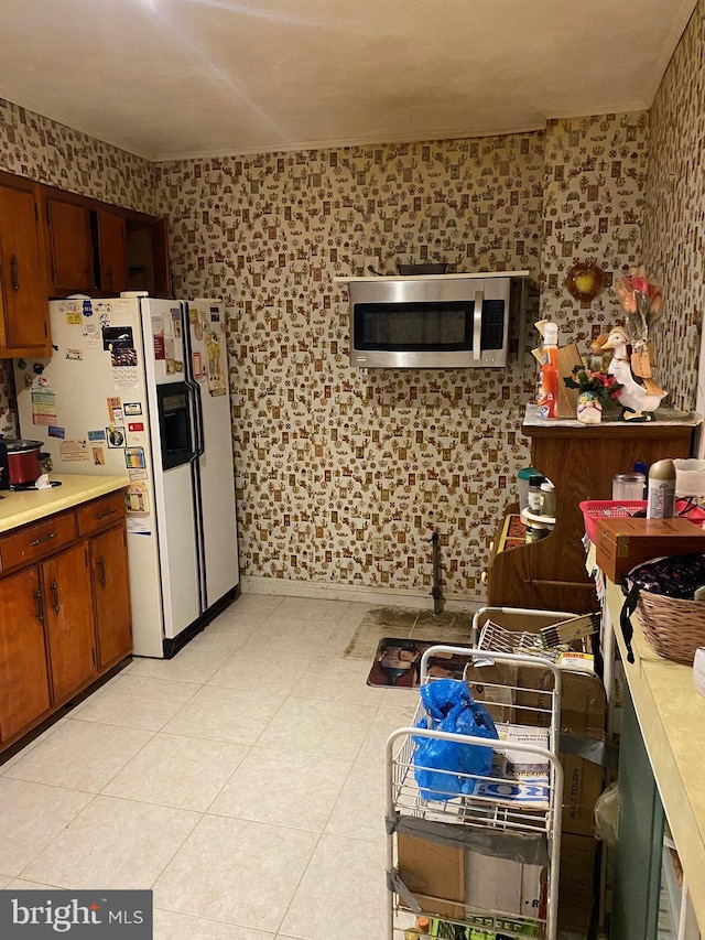 kitchen featuring light countertops, white refrigerator with ice dispenser, stainless steel microwave, and wallpapered walls