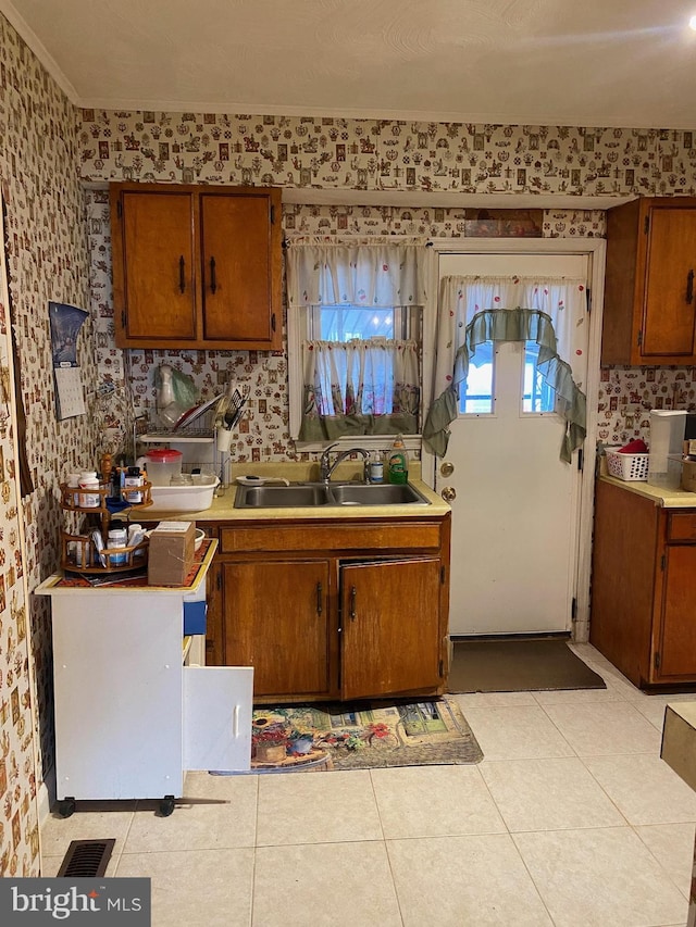 kitchen featuring light tile patterned floors, wallpapered walls, light countertops, and a sink