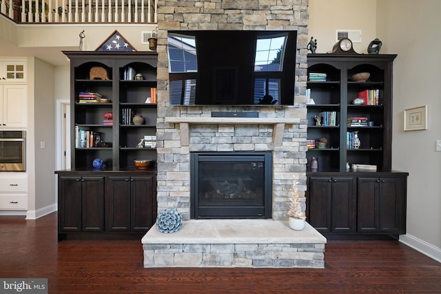 living area with dark wood-style floors, a stone fireplace, visible vents, and baseboards