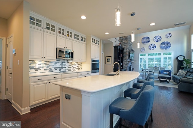 kitchen featuring glass insert cabinets, a kitchen island with sink, appliances with stainless steel finishes, and light countertops