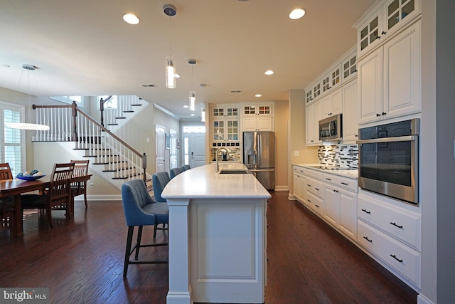 kitchen featuring white cabinetry, light countertops, appliances with stainless steel finishes, an island with sink, and pendant lighting