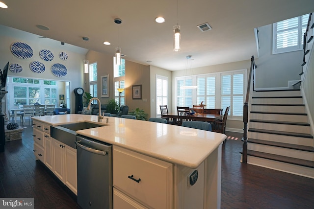 kitchen with open floor plan, a kitchen island with sink, stainless steel dishwasher, pendant lighting, and a sink