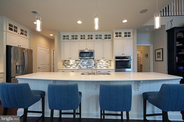 kitchen with light countertops, appliances with stainless steel finishes, a large island with sink, and glass insert cabinets