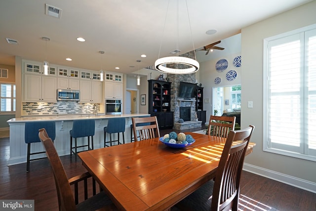 dining area with dark wood-style flooring, visible vents, a stone fireplace, and baseboards