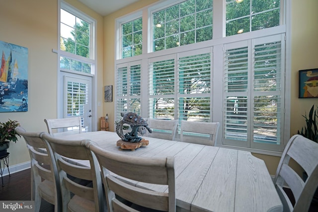 dining room with dark wood-type flooring, a towering ceiling, and baseboards