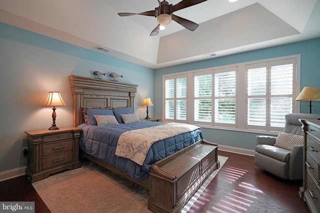 bedroom with a tray ceiling, visible vents, dark wood finished floors, and baseboards