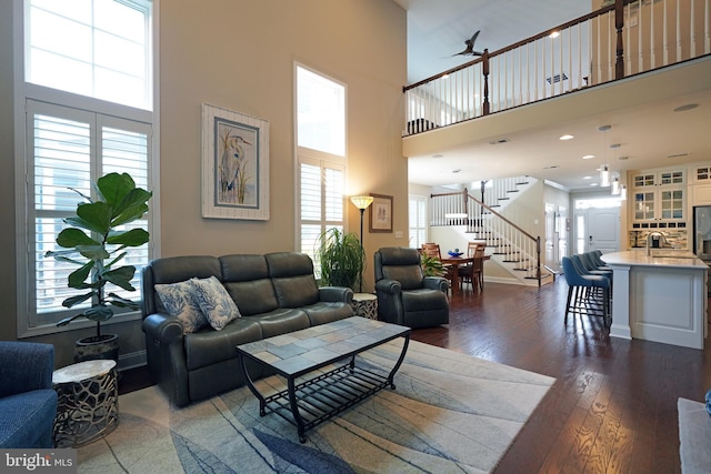 living area featuring a towering ceiling, baseboards, stairway, and dark wood-style flooring