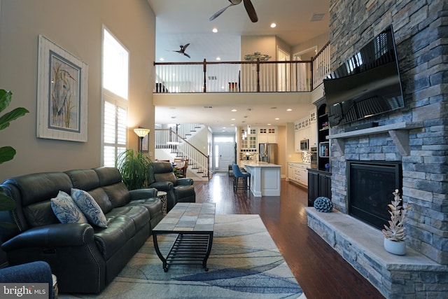 living area featuring dark wood-style flooring, a fireplace, visible vents, ceiling fan, and stairs