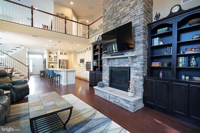 living area featuring visible vents, dark wood finished floors, a stone fireplace, and stairs