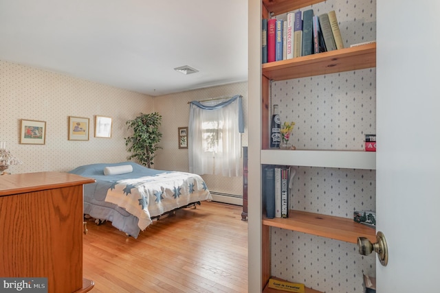 bedroom featuring light wood-type flooring, wallpapered walls, visible vents, and a baseboard heating unit