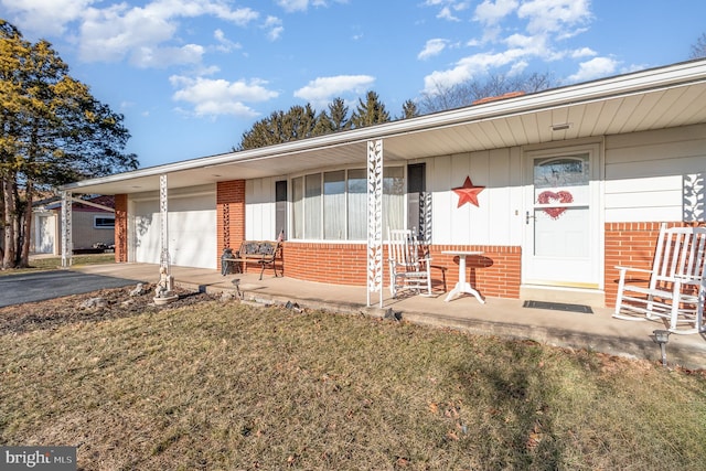 view of front of home featuring an attached garage, covered porch, brick siding, driveway, and a front yard