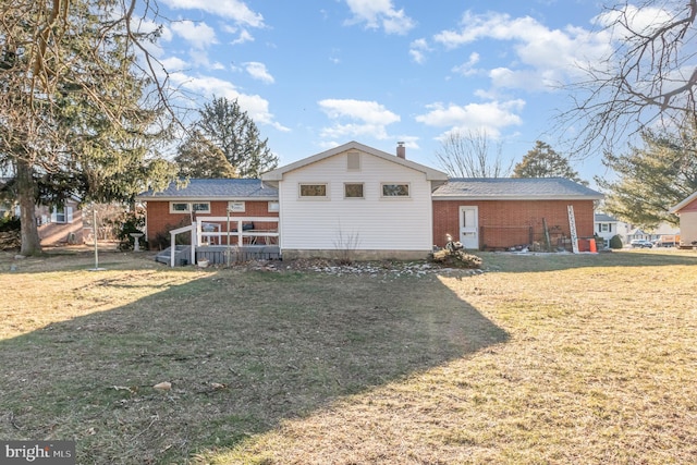 split level home featuring brick siding, a chimney, a front yard, and a wooden deck