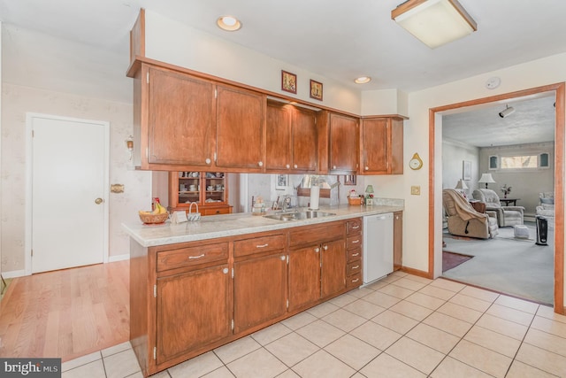 kitchen with dishwasher, brown cabinets, a peninsula, light countertops, and a sink