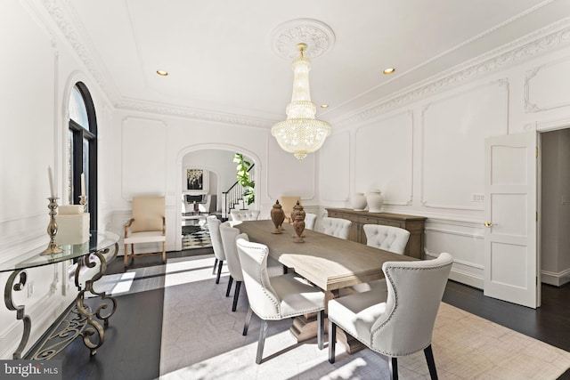 dining room with a notable chandelier, arched walkways, a decorative wall, and crown molding