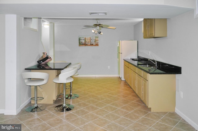 kitchen featuring ceiling fan, a sink, visible vents, freestanding refrigerator, and dark countertops