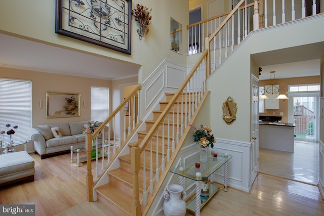 staircase with a high ceiling, ornamental molding, wood finished floors, and wainscoting