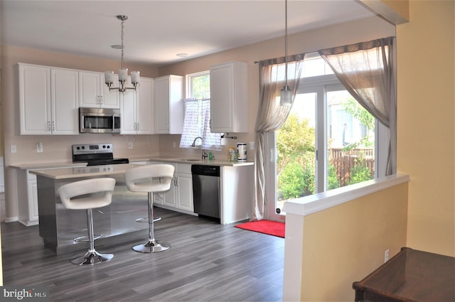 kitchen featuring decorative light fixtures, stainless steel appliances, light countertops, white cabinets, and a sink