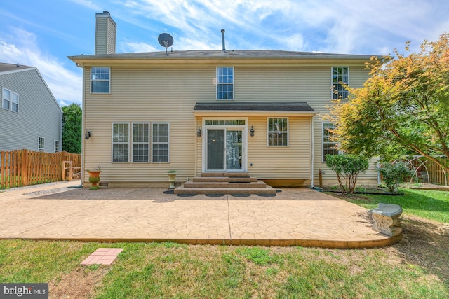 rear view of house featuring entry steps, a patio, fence, a lawn, and a chimney