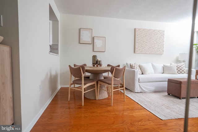 dining room with a textured ceiling, wood finished floors, and baseboards