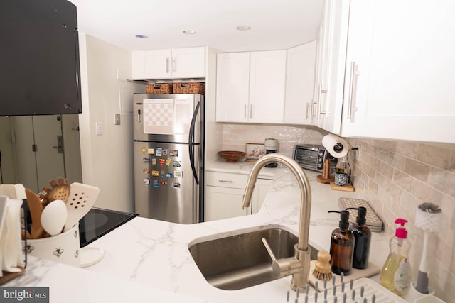 kitchen with a toaster, white cabinets, light stone counters, freestanding refrigerator, and backsplash