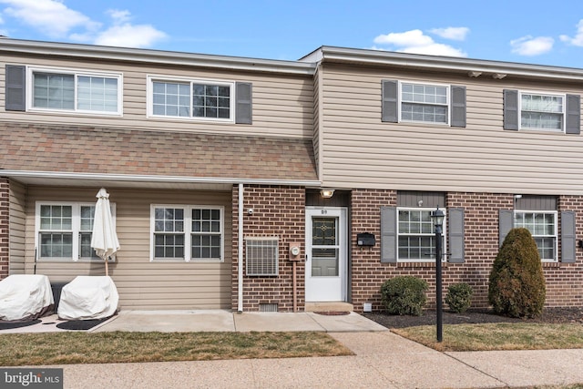 townhome / multi-family property featuring a shingled roof, a patio, and brick siding