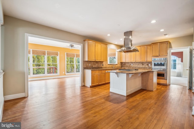 kitchen with a breakfast bar, a center island, light wood finished floors, island exhaust hood, and tasteful backsplash