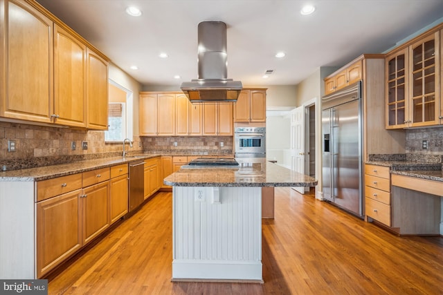 kitchen featuring island range hood, dark stone counters, a kitchen island, glass insert cabinets, and stainless steel appliances