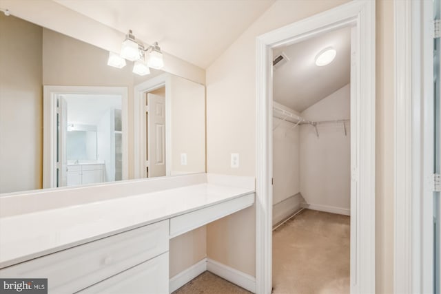 bathroom with baseboards, visible vents, lofted ceiling, a walk in closet, and vanity