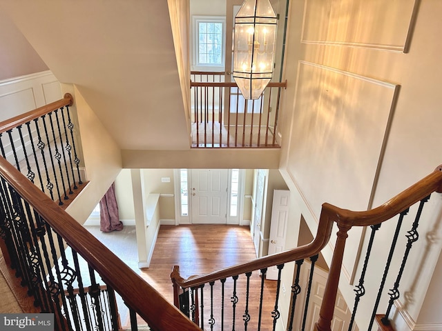 stairway with a chandelier, a wainscoted wall, a decorative wall, and wood finished floors