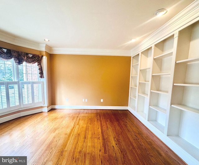 empty room with ornamental molding, built in features, baseboards, and wood finished floors