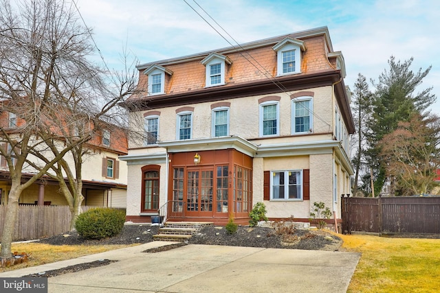 second empire-style home featuring stucco siding, fence, and mansard roof