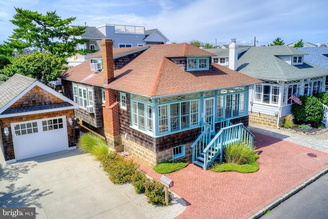 shingle-style home with a shingled roof, decorative driveway, an outdoor structure, and a chimney