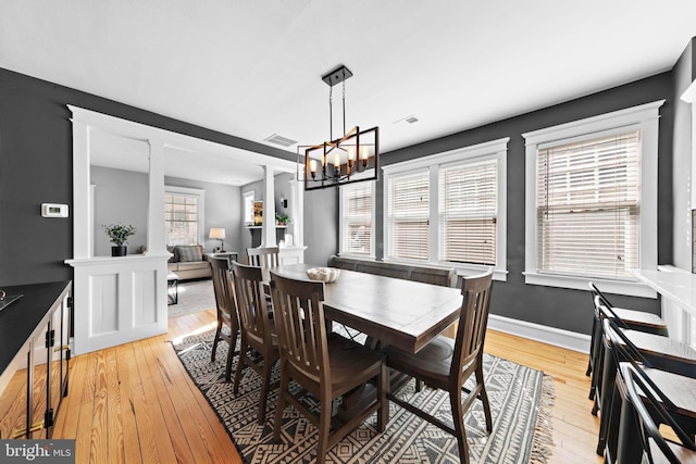 dining area featuring light wood-style floors, baseboards, visible vents, and ornate columns