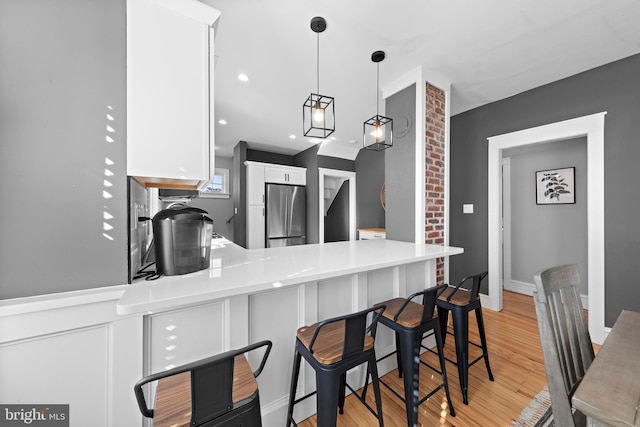 kitchen featuring light countertops, freestanding refrigerator, white cabinetry, light wood-type flooring, and a peninsula