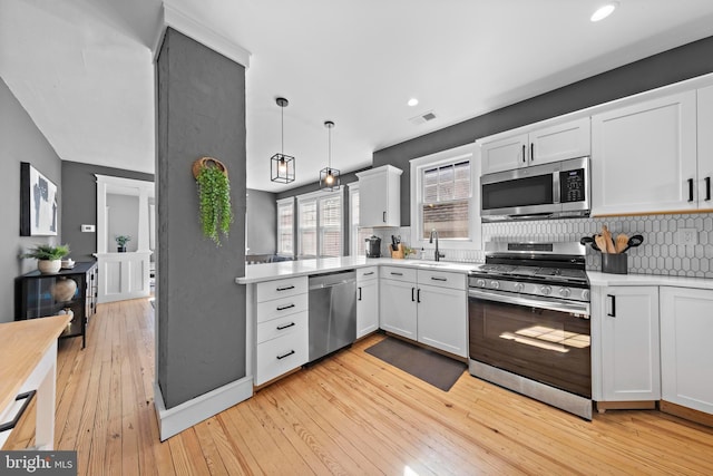 kitchen with stainless steel appliances, light countertops, hanging light fixtures, and white cabinetry