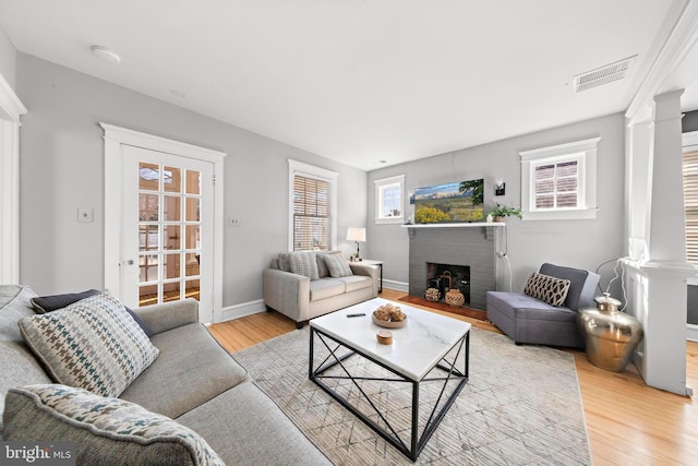 living area with light wood-type flooring, decorative columns, a fireplace, and visible vents