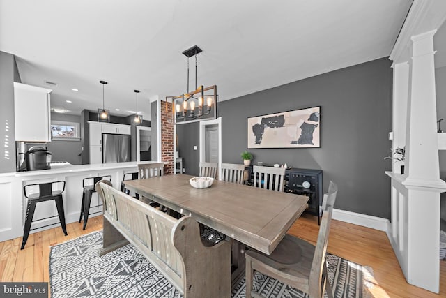 dining area with light wood-type flooring, decorative columns, baseboards, and an inviting chandelier