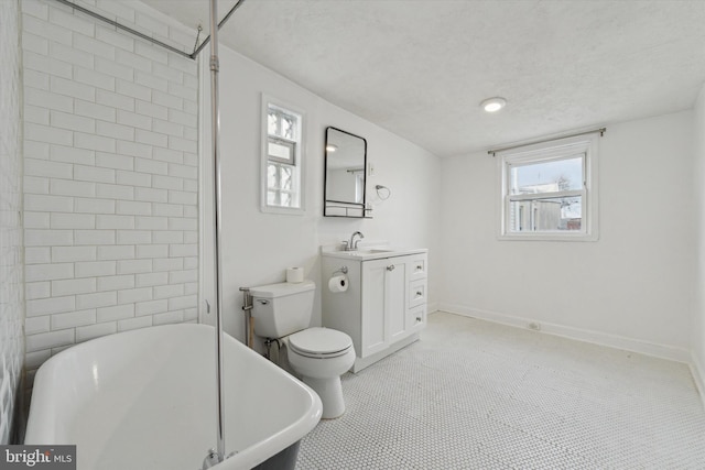 bathroom featuring a freestanding bath, toilet, a textured ceiling, vanity, and baseboards