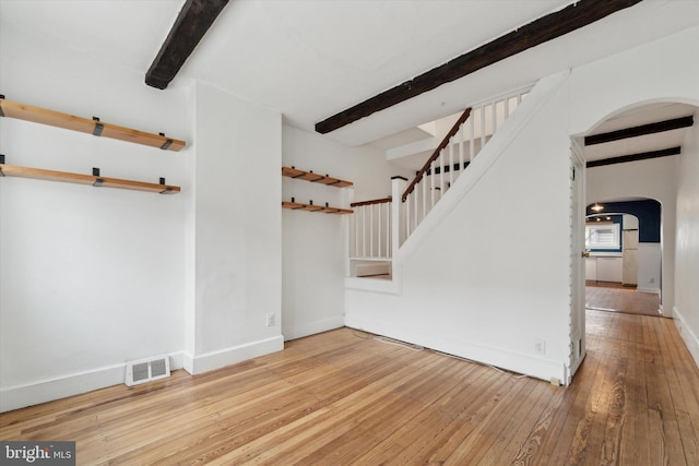 empty room with arched walkways, stairway, beam ceiling, and light wood-style floors