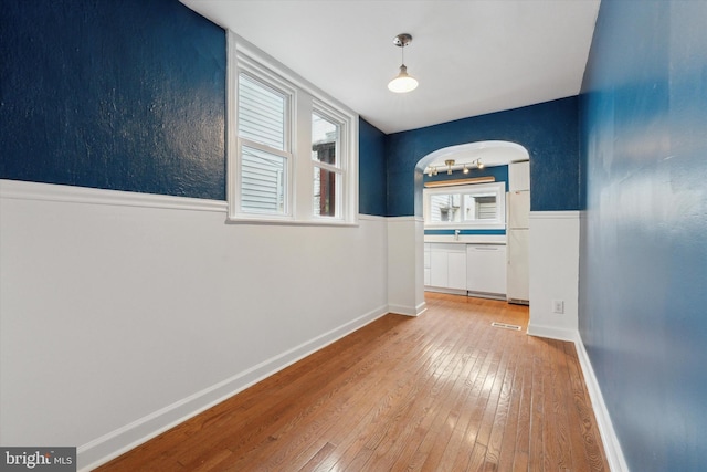 hall with arched walkways, wood finished floors, and baseboards