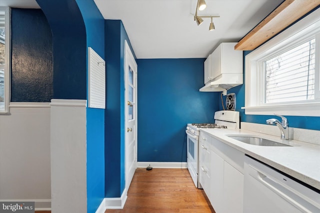 kitchen with white appliances, white cabinets, light countertops, light wood-type flooring, and a sink