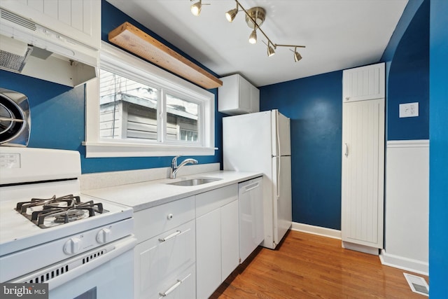 kitchen featuring white appliances, white cabinets, light countertops, under cabinet range hood, and a sink