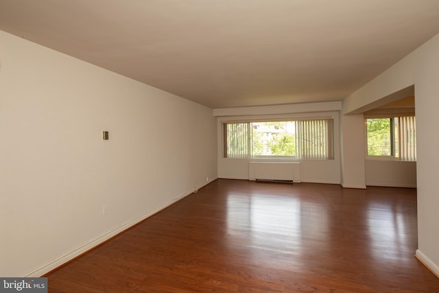 empty room featuring radiator, a wealth of natural light, baseboards, and dark wood-style flooring