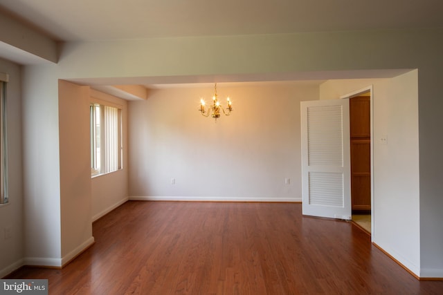 empty room featuring baseboards, wood finished floors, and a chandelier