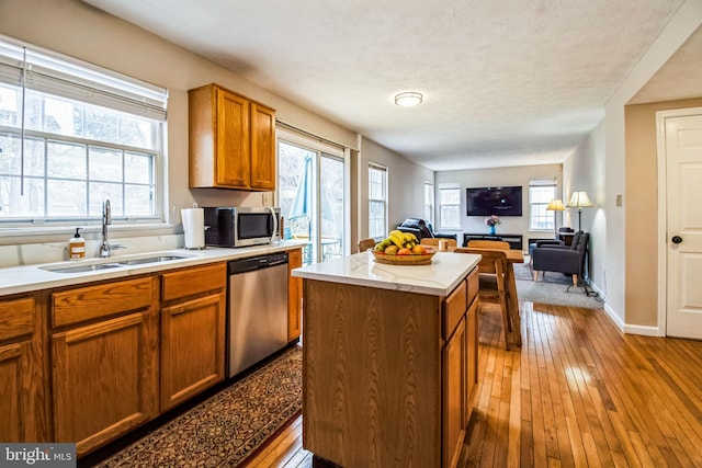 kitchen with stainless steel appliances, light countertops, open floor plan, a sink, and a kitchen island