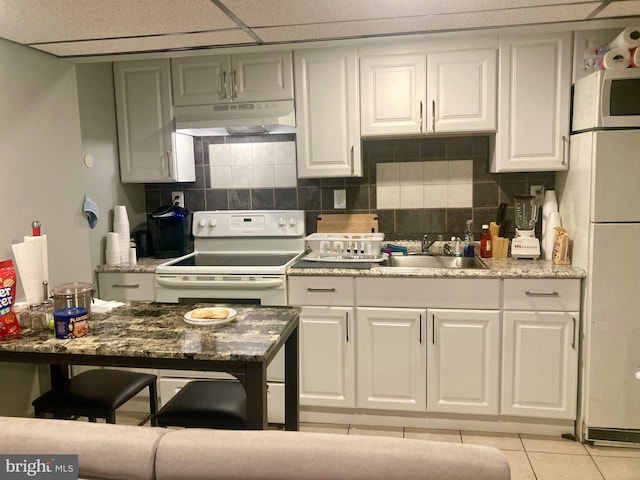 kitchen with decorative backsplash, light tile patterned flooring, white cabinets, white appliances, and under cabinet range hood