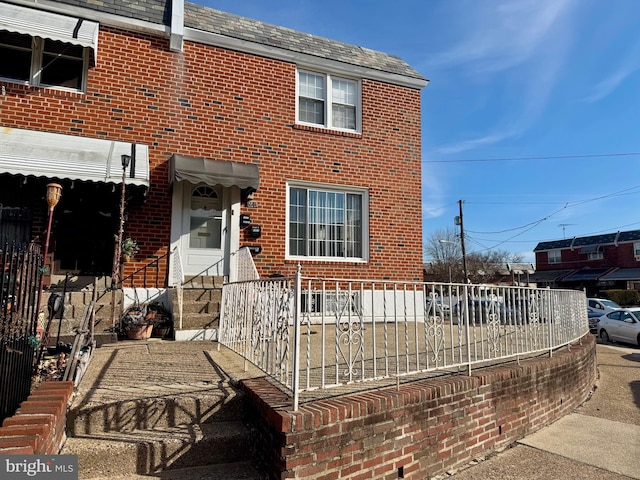 multi unit property featuring entry steps, brick siding, a shingled roof, and fence