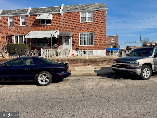 view of property featuring a high end roof, fence, mansard roof, and brick siding