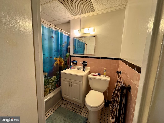 full bathroom with a wainscoted wall, tile walls, a paneled ceiling, toilet, and vanity